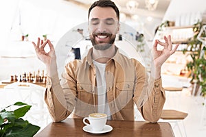 Young bearded man sits in cafe in yoga position drinking coffee during lunch break, calm concept