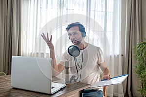 Young bearded man sitting in headphones and speaking in microphone