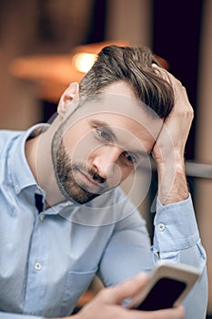 Young bearded man sitting at the table and looking anticipated