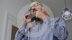 Young bearded man sitting and using phone at living room. Close up of the young man with a beard talking on the phone in the livin