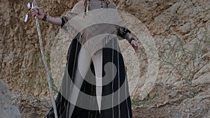 A young bearded man with a staff in his hands in the clothes of a shaman prays on a rock among the sandy dunes of the