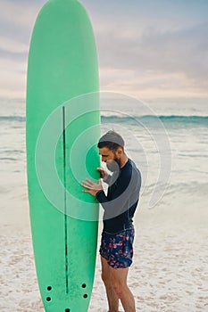 Young bearded man with surfboard standing near a beach. Man with surfing board outdoors on a summer day.