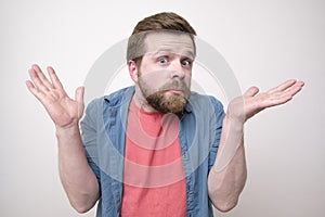 Young, bearded man is surprised and puzzled, and raises his hands in confusion. Isolated on white background