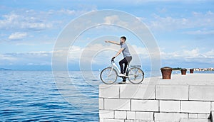 Young bearded man tourist on bicycle on high paved stone sidewalk enjoying clear blue sea water