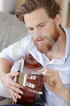 Young bearded man tuning guitar