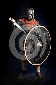 Young bearded man in a Viking-era helmet standind and holding a sword and shield