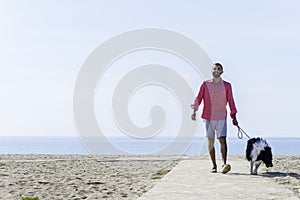 Young bearded man walking with his dog tied up on the beach