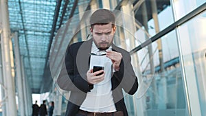 Young bearded man walks through the airport terminal, notices smth on his phone, takes off the sunglasses in surprise