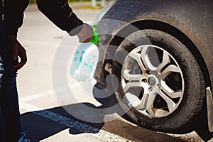Young bearded man washes his car`s wheel rims, spraying water from spray