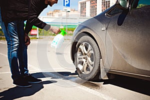 Young bearded man washes his car`s wheel rims, spraying water from spray