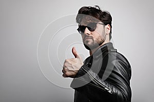 Young bearded man wearing biker jacket posing at the white background. Horizontal.