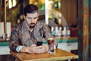 Young bearded man wearing casual clothes looking at his smartphone in a modern pub