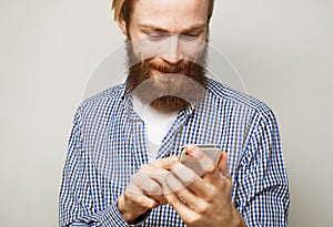 Young bearded man wearing casual shirt typing sms on gray background