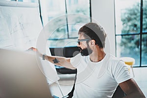 Young bearded man wearing eye glasses and working at sunny office.Blurred background. Horizontal. photo