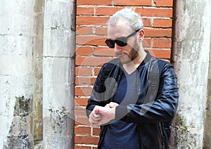 A young bearded man wearing sunglasses and looking on the watch.