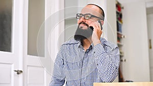 Young bearded mn sitting and using phone at living room. Close up of the young man with a beard talking on the phone in the livin
