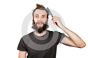 Young bearded overgrown man holding comb and combing his hair. Isolated on white background