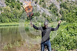 young bearded rock musician screaming, raised up his hands with a burning guitar. backdrop of a bright summer landscape photo