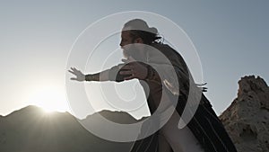 A young bearded shaman prays against the backdrop of sunset among the sand dunes of the desert