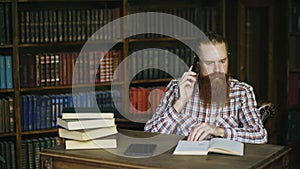 Young bearded student talking phone while preparing for exams in univercity library photo