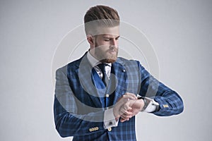 Young bearded stylish businessman leader indoors dressed in three-piece suit checking the time on his watch. isolated on grey