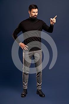 Young bearded stylish teacher or business man pointing finger side. Full body length portrait isolated on Pacific Blue studio