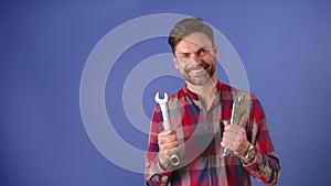 Young bearded unconfident man holding tools and smiles . Isolated