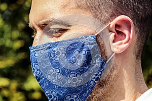 Young bearded white man with a blue fabric face mask during coronavirus pandemic. Coronavirus, COVID-19 outbreak. Virus protection