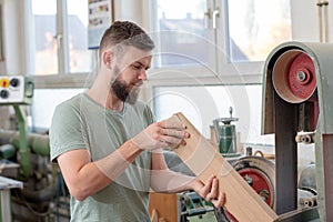 Young bearded worker in a carpenter`s workshop using grinding machine