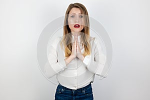 Young beatuiful blond woman standing in praying position, looking innocent on isolated white background , body language concept
