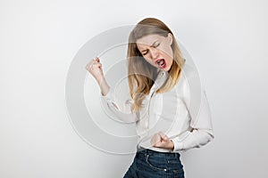 Young beatuiful blond woman standing in winning position clenching her fists looking happy on isolated white background, body