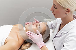 Young beautician or dermatologist doing manual facial cleansing for a woman in a beauty salon. Spa facial massage