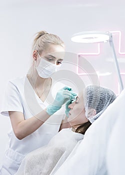 The young beautician doctor preparing to making injection in female forehead. The doctor cosmetologist makes anti-aging treatment