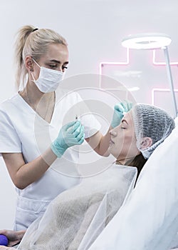 The young beautician doctor preparing to making injection in female forehead. The doctor cosmetologist makes anti-aging treatment