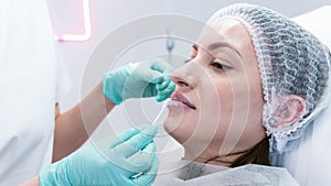 The young beautician doctor preparing to making injection in female lips. The doctor cosmetologist makes lip augmentation