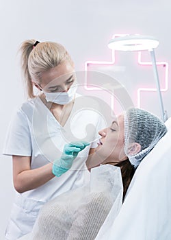 The young beautician doctor preparing to making injection in female lips. The doctor cosmetologist makes lip augmentation