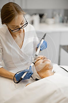 Young beautician doing microcurrent therapy on face