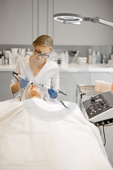 Young beautician doing microcurrent therapy on face