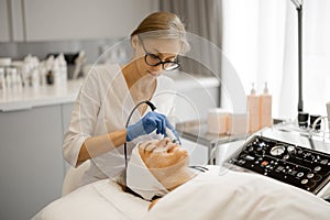 Young beautician doing microcurrent therapy on face