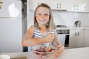 Young beautiful and adorable girl 6 or 7 years old cooking and baking at home kitchen preparing strawberry cake with bowl smiling