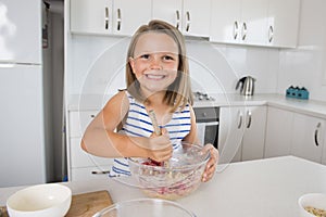 Young beautiful and adorable girl 6 or 7 years old cooking and baking at home kitchen preparing strawberry cake with bowl smiling