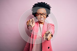 Young beautiful African American afro businesswoman with curly hair wearing pink jacket pointing to you and the camera with