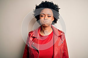 Young beautiful African American afro woman with curly hair wearing casual red jacket puffing cheeks with funny face