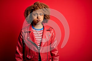 Young beautiful African American afro woman with curly hair wearing casual red jacket puffing cheeks with funny face