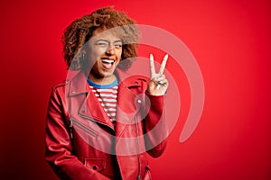 Young beautiful African American afro woman with curly hair wearing casual red jacket smiling with happy face winking at the
