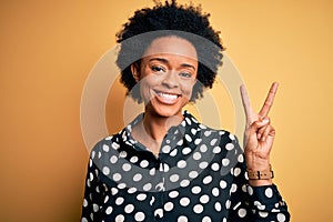 Young beautiful African American afro woman with curly hair wearing casual shirt standing smiling with happy face winking at the