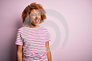 Young beautiful African American afro woman with curly hair wearing casual striped t-shirt winking looking at the camera with sexy