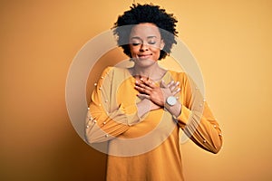 Young beautiful African American afro woman with curly hair wearing casual t-shirt smiling with hands on chest with closed eyes