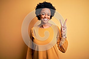 Young beautiful African American afro woman with curly hair wearing casual t-shirt smiling with happy face winking at the camera