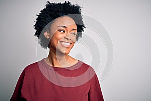 Young beautiful African American afro woman with curly hair wearing casual t-shirt standing looking away to side with smile on